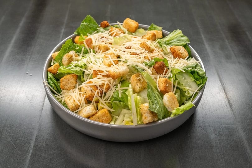 Fresh Caesar salad with crisp romaine lettuce, crunchy croutons, and shredded Parmesan cheese in a gray bowl.