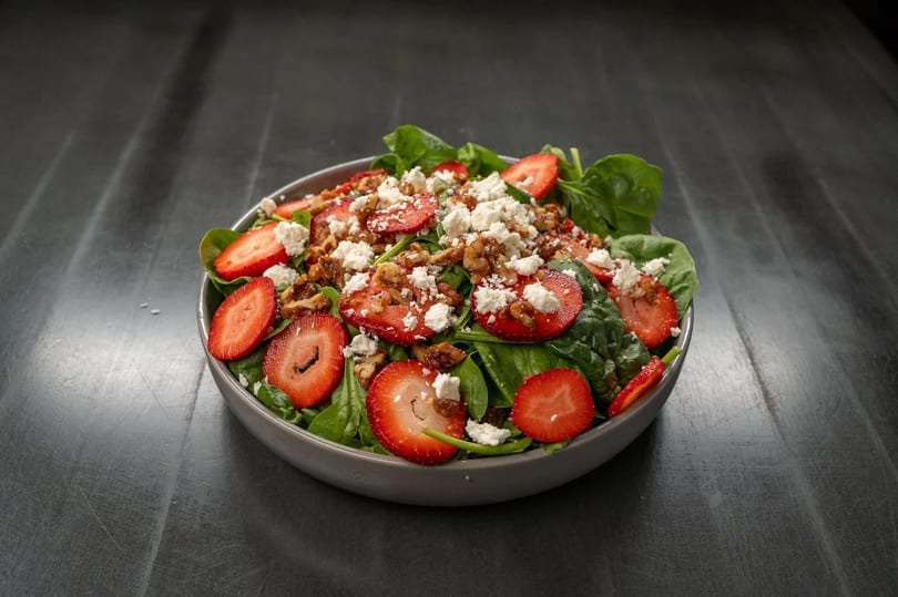 Spinach salad with sliced strawberries, crumbled feta cheese, and walnuts in a gray bowl.