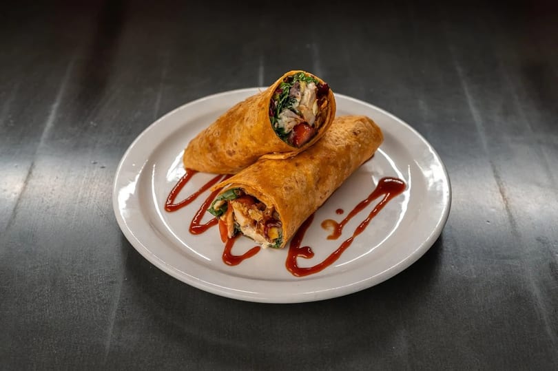 Two chicken wraps with vegetables and sauce on a white plate.